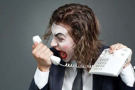 Portrait of businessman with theatrical makeup shouting at telephone receiverの写真素材