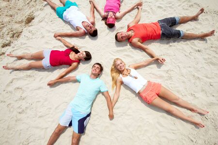 Six friends lying on sand in circle の写真素材