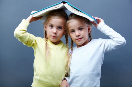 Portrait of lovely twin girls holding open book over headsの写真素材