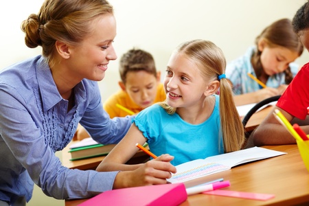 Portrait of smart girl and her teacher looking at each other at lesson in classroomの写真素材