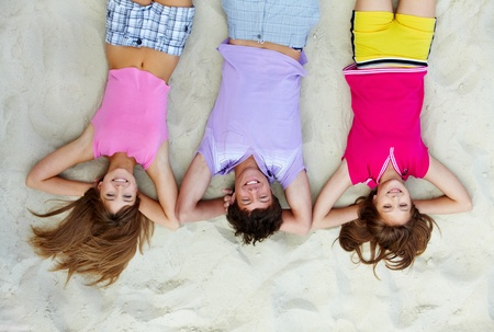 Above angle of laughing teenage friends lying on sandy beachの写真素材