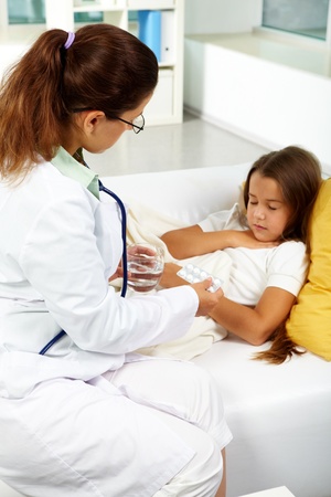 Portrait of clinician in eyeglasses with tablets looking at sick girl lying near byの写真素材
