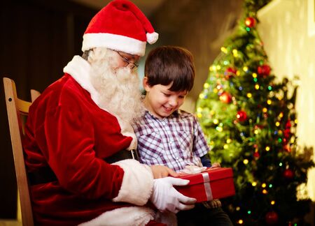 Photo of cute boy and Santa Claus holding giftbox and looking at itの写真素材