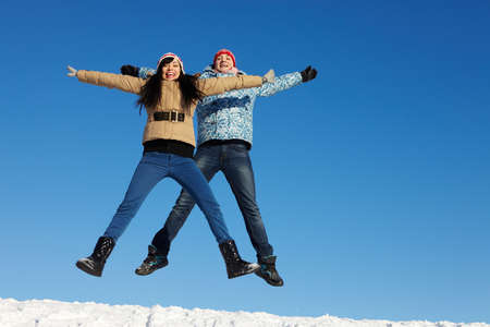 Portrait of happy couple in warm clothes jumping and looking at camera 
