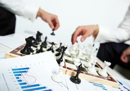 Image of two bishops on business papers with human hands playing chess on backgroundの写真素材