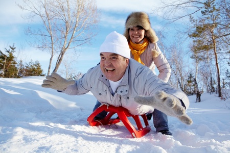 Portrait of happy mature couple riding on sledge in winterの写真素材