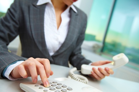 Female hand holding phone receiver and dialing number