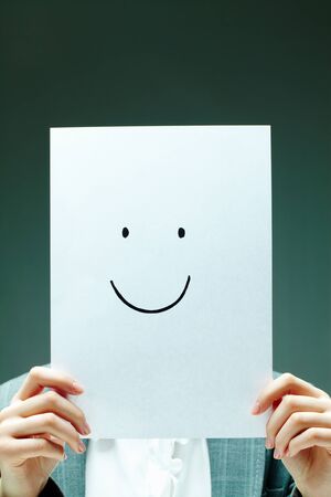 Image of female holding paper with drawn smile in front of her faceの写真素材
