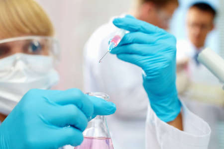 Female scientist looking at substance dropping from syringe