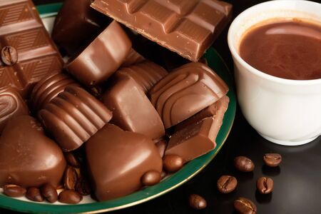 Close-up of cappuccino in porcelain cup, lots of various chocolates and coffee grains near by