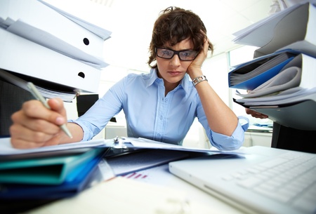 Perplexed accountant doing financial reports being surrounded by huge piles of documentsの写真素材