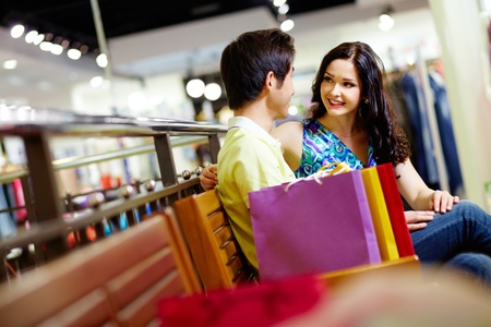 Cute couple sitting on a bench in the shopping mall and admiring each otherの写真素材