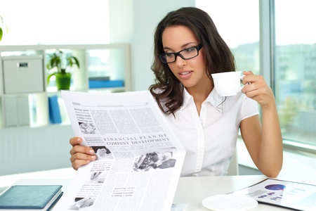 Portrait of a business lady reading newspaper and drinking coffee in the morningの写真素材