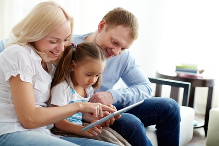 Portrait of happy parents with their daughter sitting on sofa with digital tablet