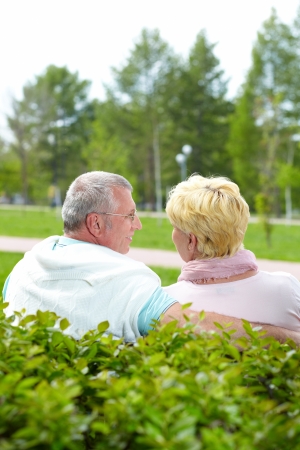 Mature couple sitting and talking in park in summerの写真素材