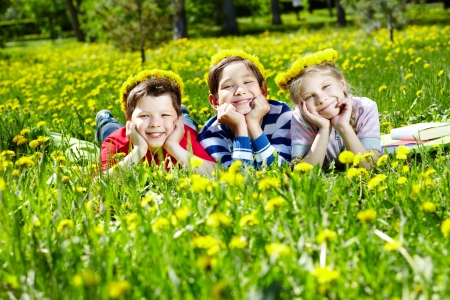 Three children with dandelion wreaths having rest on grass の写真素材