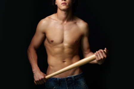 Close-up of shirtless man with bat over black backgroundの写真素材