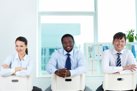 Portrait of successful business team sitting on chairs and looking at cameraの写真素材