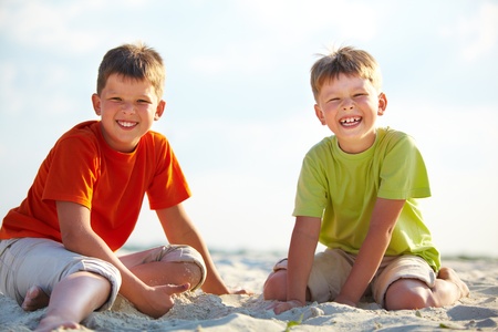 Photo of happy siblings sitting on sand on summer vacationの写真素材