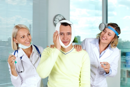 Portrait of two careful female doctors giving first aid to male patient with toothache in hospitalの写真素材