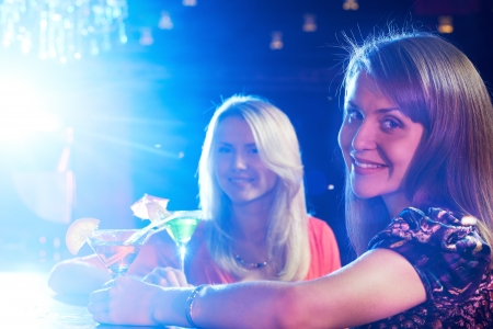 Portrait of happy girlfriends holding martini glasses with cocktails in barの写真素材