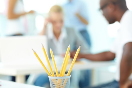 Close-up of several pencils in plastic glass on background of group of students workingの写真素材