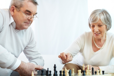 Portrait of senior woman pointing at chess-man while playing chess at leisure with her husband near byの写真素材