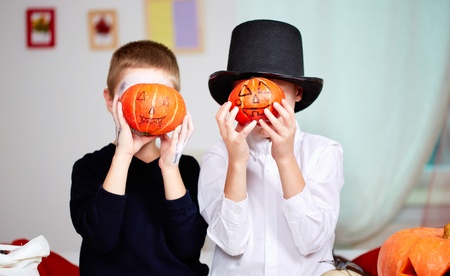 Photo of twin eerie boys holding Halloween pumpkins in front of their faces の写真素材