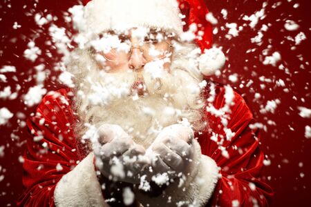 Photo of Santa Claus in eyeglasses blowing snow from his palmsの写真素材