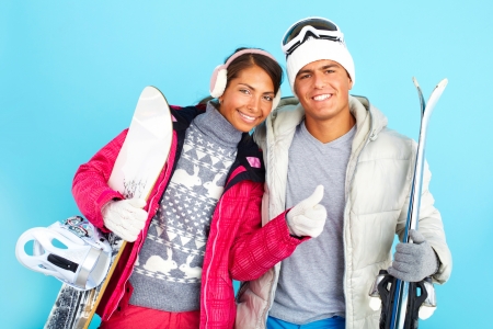 Portrait of happy girl and handsome man in winterwear holding snowboard ans skisの写真素材