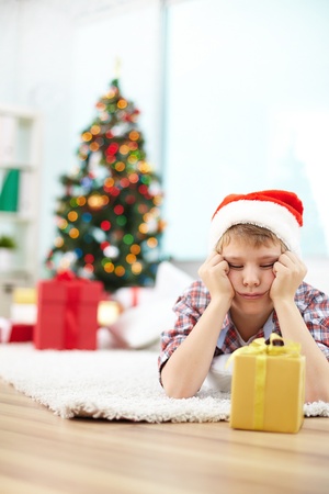 Portrait of bored boy looking at giftbox while lying on the floor on Christmas eveningの写真素材
