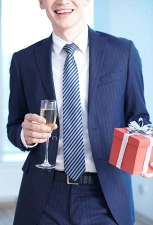 Close-up of businessman in suit holding flute of champagne and giftboxの写真素材