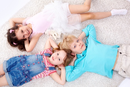 Three kids lying on the floor and looking at cameraの写真素材