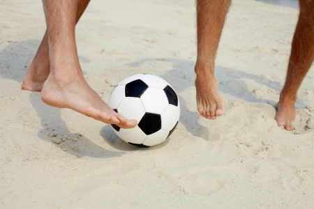 Close-up of male foot playing football on sandの写真素材