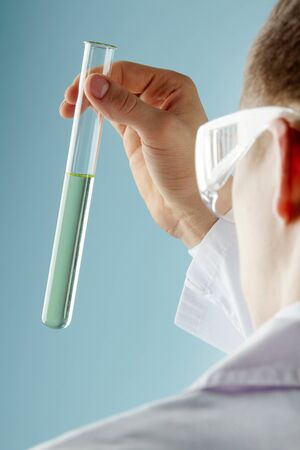 Male scientific worker looking at a semi-transparent chemical in a glass tubeの写真素材