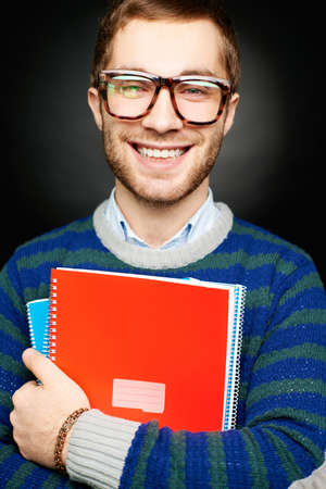 Portrait of happy student in eyeglasses holding copybooks and looking at camera with smileの写真素材