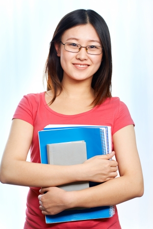Portrait of happy student in eyeglasses holding books and looking at camera with smileの写真素材
