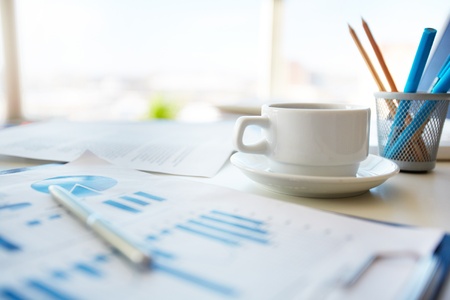 Close-up image of an office desk at morning with a cup of tea and financial documentsの写真素材