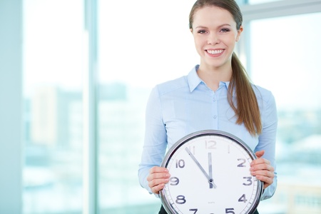 Portrait of happy businesswoman holding clock and looking at camera