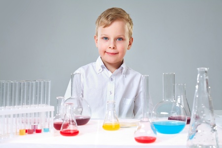 A little boy looking at camera with liquids in flasks near by