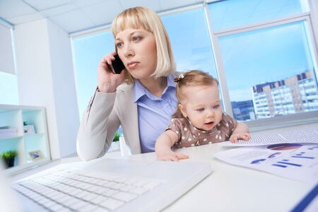 Portrait of successful businesswoman at workplace calling with her baby near byの写真素材