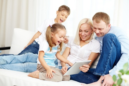 Portrait of happy family with touchpad laughing at something funny while sitting on sofa 