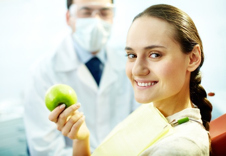 Smiling woman with apple looking at camera with dentist on backgroundの写真素材