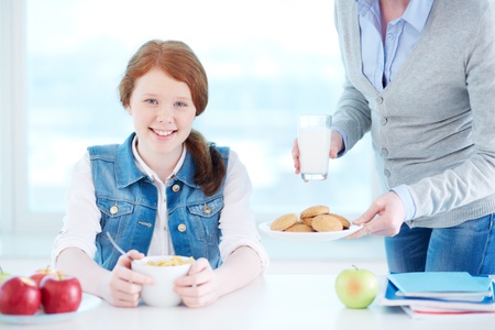 Lovely girl looking at camera while her mother near by offering her some snackの写真素材