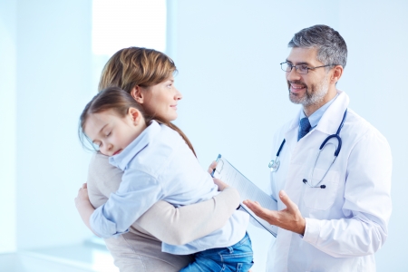 Young woman holding her little sleeping daughter while speaking to the doctor in hospitalの写真素材