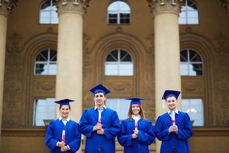 Group of smart students in graduation gowns holding certificates