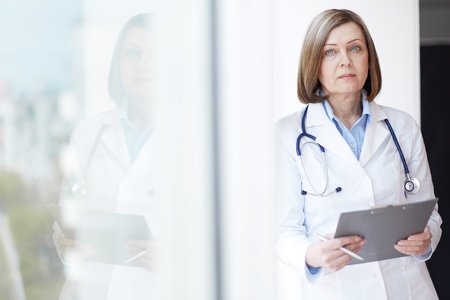 Portrait of pretty female practitioner with clipboard looking at cameraの写真素材