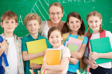 Portrait of cute schoolchildren looking at camera with their teacher among them の写真素材