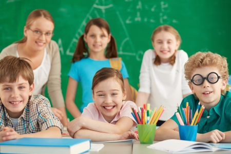 Portrait of cute schoolchildren looking at camera with their teacher and classmates on background の写真素材
