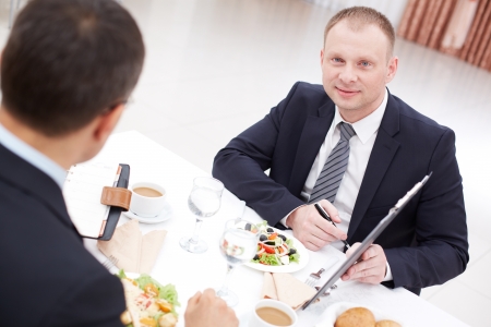 Confident businessman with clipboard looking at camera during paper discussion at business lunchの写真素材